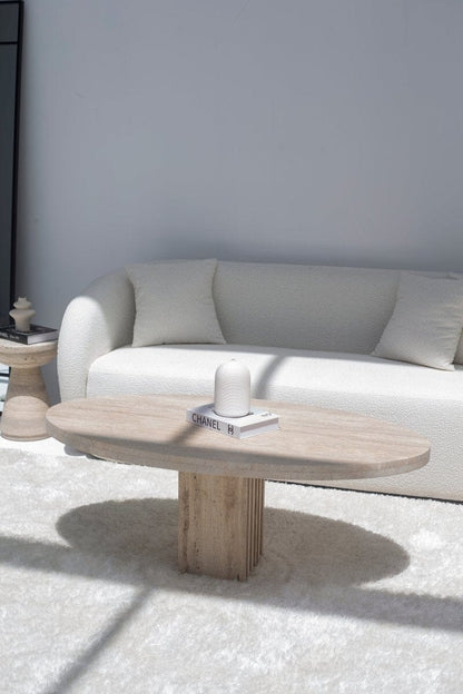 Table basse ovale en travertin devant un canapé blanc