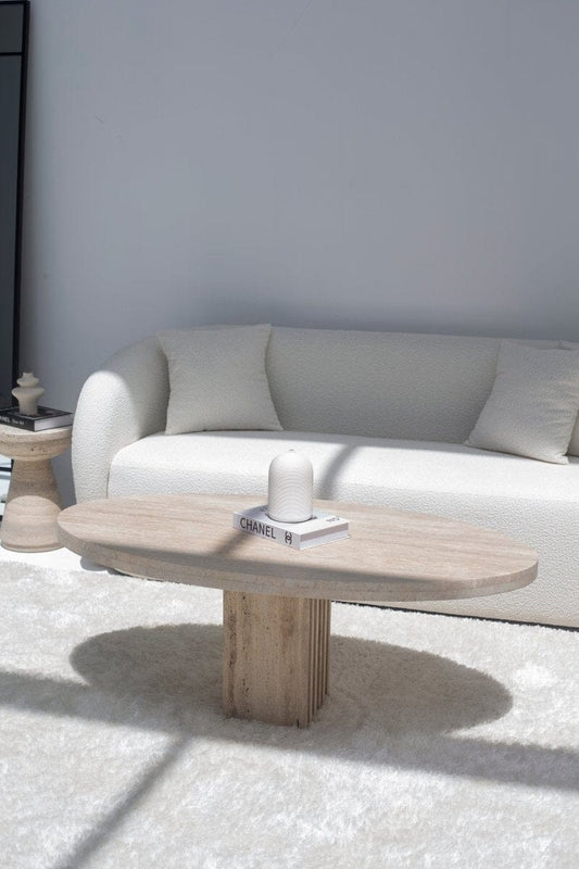 Table basse ovale en travertin devant un canapé blanc